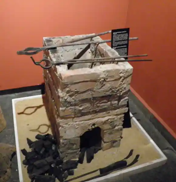 Rectangular grill made from clay bricks with metal tongs, and coals.